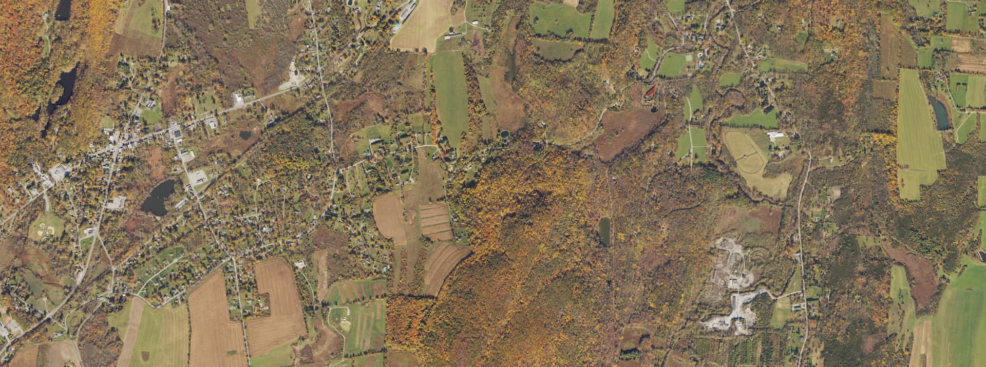 Aerial survey view over Amenia, NY, showing the hamlet centre, farm fields and wooded ridges